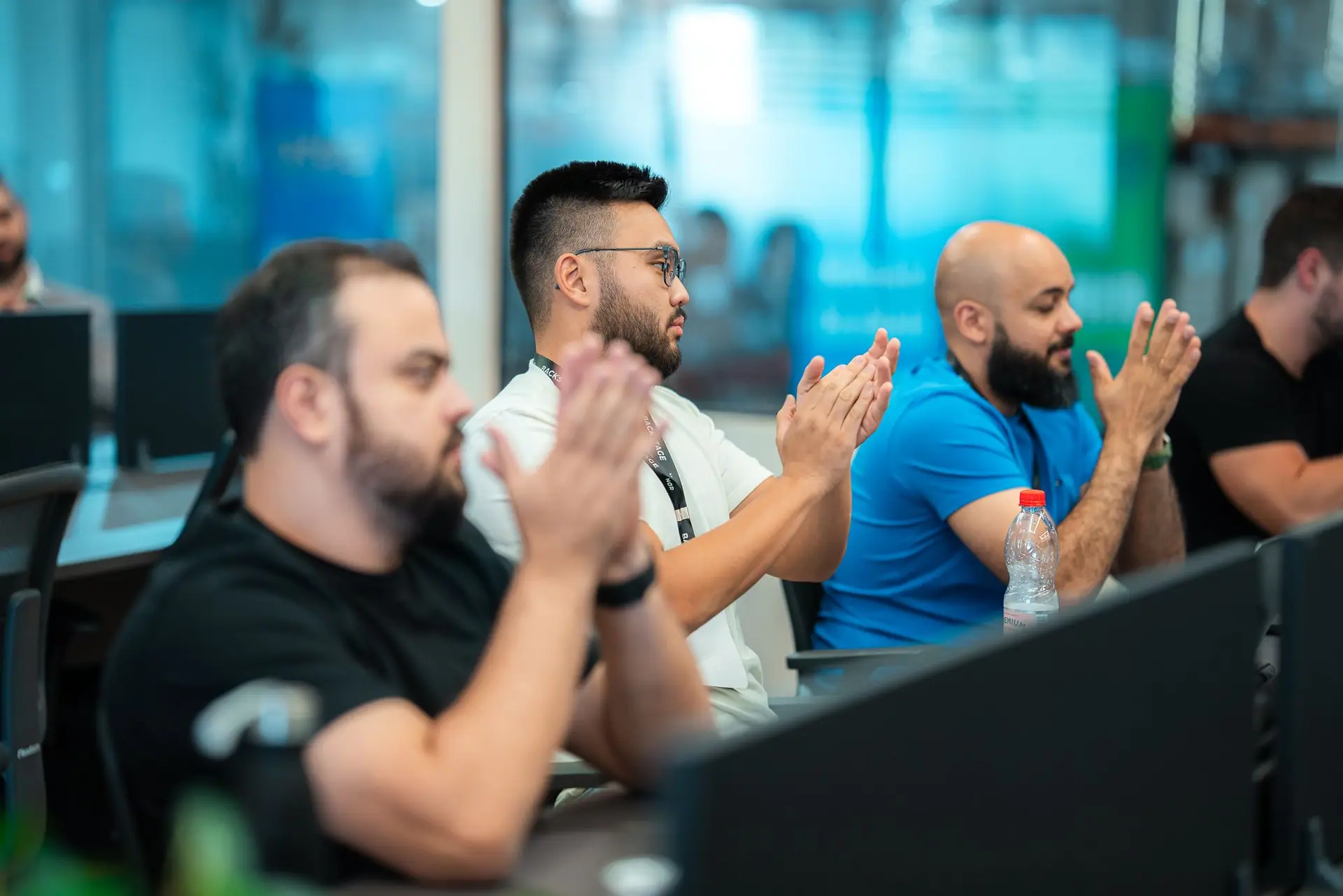 Participantes aplaudindo sentados às bancadas da sala de reuniões.