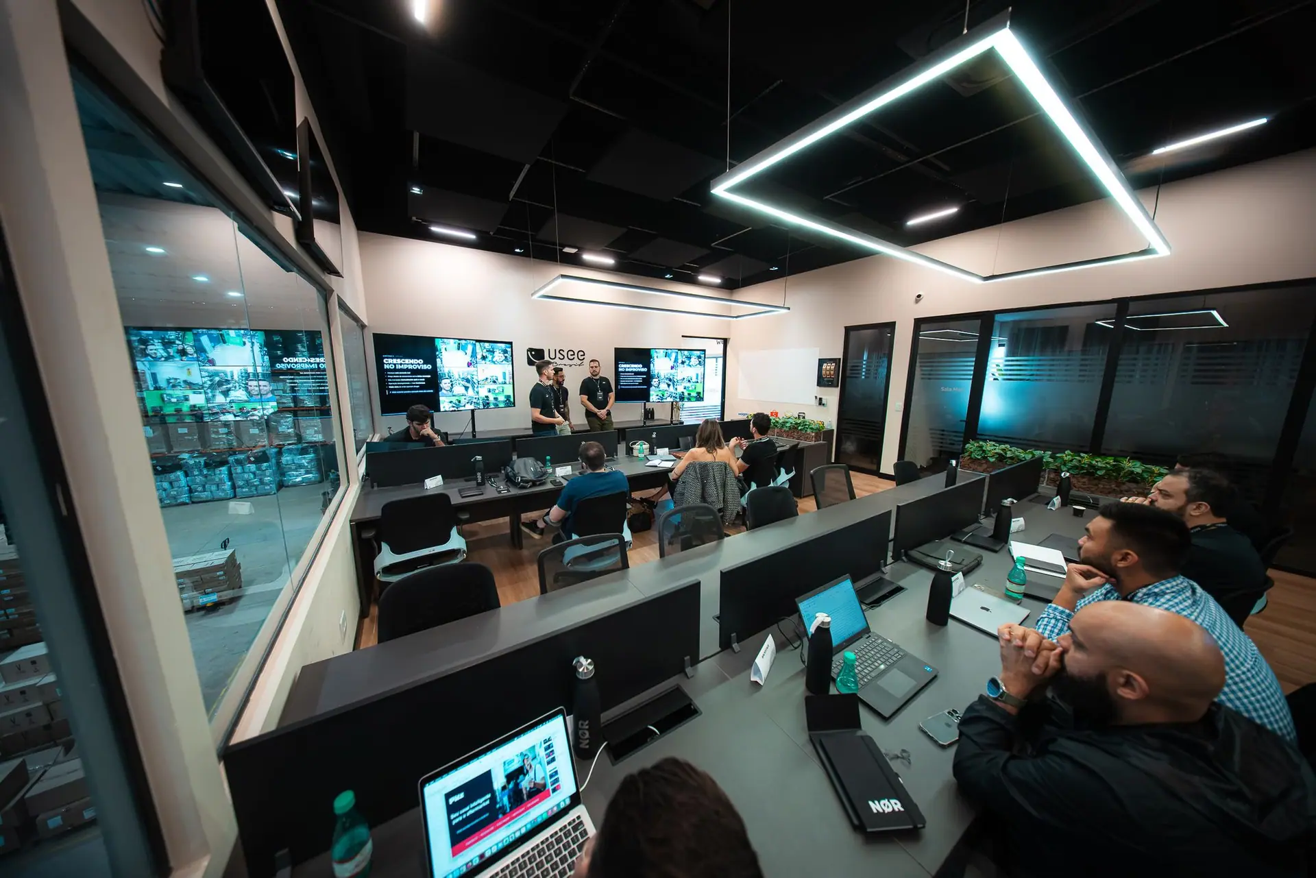 Sala de reuniões da Usee Brasil com participantes sentados diante de três apresentadores.